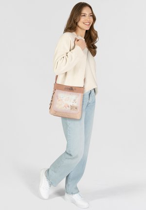 Umhängetasche aus weichem pinkem Material, mit einem gemusterten Vorderteil, das Kunst und Text zeigt. Sie verfügt über einen verstellbaren Tragegurt und dezente Hardware-Details.