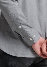 Graues und weiß kariertes Hemd zum Knöpfen mit langen Ärmeln, das eine glatte Textur und kontrastierende weiße Knöpfe an den Manschetten aufweist.