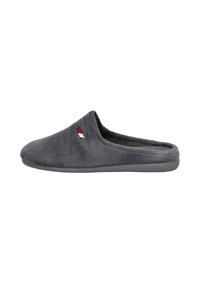 Zapatilla de tela suave y gris, tipo pantufla, con punta cerrada y parte trasera abierta, y un pequeño detalle bordado en rojo, blanco y negro en el lateral.