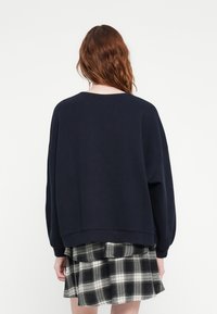 Sweatshirt oversized bleu marine à manches longues et col rond, associé à une mini-jupe à carreaux noir et blanc avec des couches volantes.