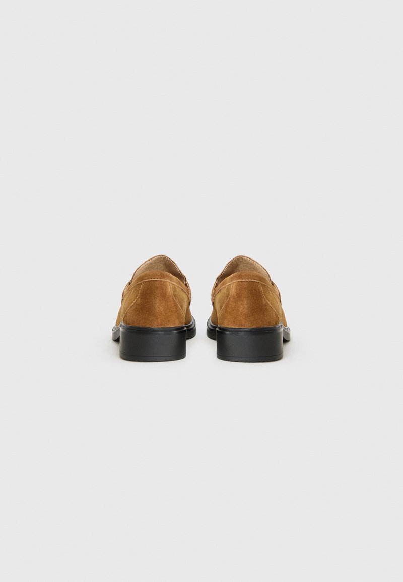 Braune Wildlederschuhe mit schwarzen Sohlen, von hinten betrachtet, zeigen ein einfaches, elegantes Design vor einem weißen Hintergrund.