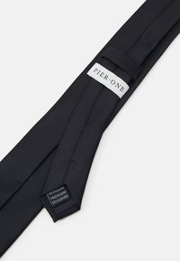 Cravate en polyester noir, avec une texture lisse, un design droit et une boucle pour un maintien sécurisé. L'étiquette indique "PIER.ONE". Nettoyage à sec seulement.