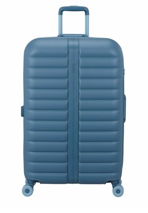 Valise rigide bleue avec des rainures horizontales, quatre roues pivotantes et une poignée télescopique déployée.