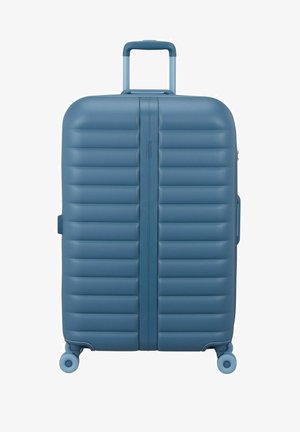 Valise rigide bleue avec des rainures horizontales, quatre roues pivotantes et une poignée télescopique déployée.