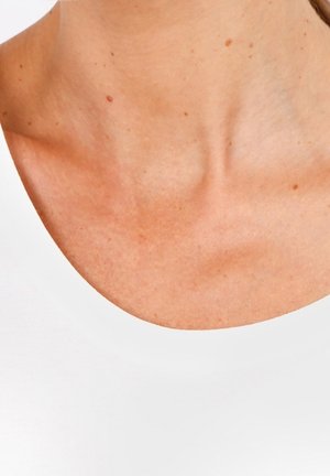 Gros plan sur la clavicule et le haut de la poitrine d'une personne à la peau claire, portant un haut blanc sans manches.