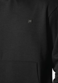 Felpa nera con cappuccio realizzata in tessuto morbido, caratterizzata da un piccolo logo ricamato sul petto, una tasca a marsupio e polsini a costine.