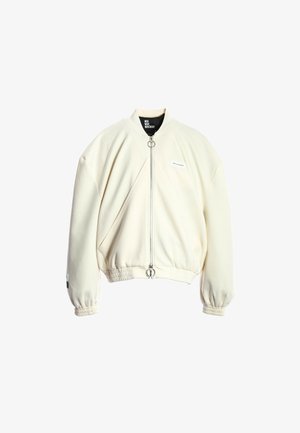 Chaqueta bomber crema hecha de una tela suave, con un cierre frontal de cremallera y anilla en la pestaña, puños elásticos y un diseño de ajuste relajado.