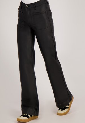 Zwarte faux leren broek met een rechte snit, voorzien van twee zijzakken en contrasterende stiksels. Gemaakt in combinatie met casual sneakers.