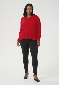 Blusa roja de manga larga con escote en V y un corte holgado, combinada con jeans skinny negros y mules negros de tacón. Diseño simple, textura suave.