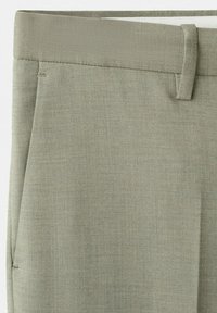 Close-up of gray-green tailored pants showing waistband, belt loop, and side pocket seam.