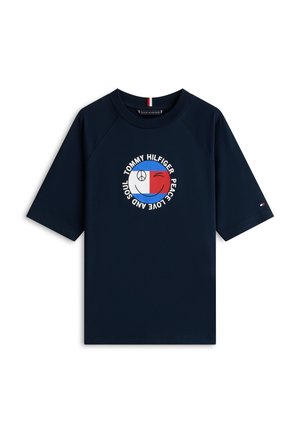 Camiseta de manga corta azul marino con un logo circular en rojo, blanco y azul que presenta un símbolo de la paz, una cara guiñando un ojo y el texto "Tommy Hilfiger Peace Love and Soul".