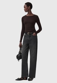 Bruine langemouwen top gecombineerd met hoge taille, wijde zwarte denim jeans. Model houdt een zwarte handtas vast; de schoenen hebben een gouden accent.