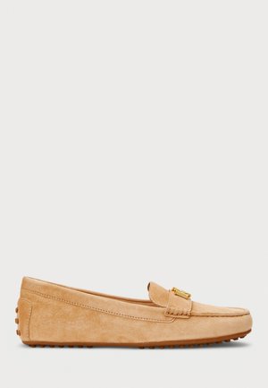 Beige ruskindslipper med lav hæl, gummisåle med nitter og en guldfarvet metalspænde i toppen foran.
