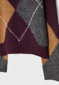 Ourlet et poignets de pull en tissu de laine avec motif argyle en bordeaux, gris, moutarde, et détails de couture blanche.