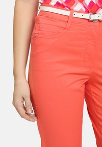 Pantalons de couleur corail en tissu lisse, avec un design ajusté, des poches latérales et une ceinture blanche avec une boucle en métal argenté.