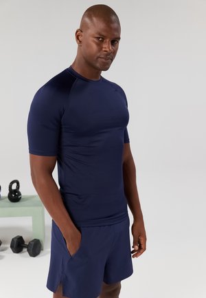 Navy short-sleeve athletic shirt made of stretchy fabric, paired with matching shorts. Features a fitted design and side pockets on shorts.