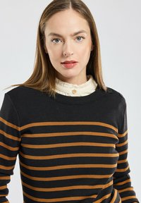 Maglione a righe nero e ruggine con trama a coste, dotato di bottoni sulle spalle e di un colletto bianco a strati con ruches sotto.
