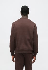 Hnedá mikina s okrúhlym výstrihom, vyrobená z bavlneného zmesi, s rebrovanými manžetami a lemom, hladkou textúrou a voľným strihom.