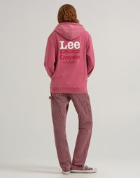 Felpa rosa con grande scritta bianca "Lee Crayola" e "Mulberry." Abbinata a pantaloni a righe rosa e rossi. Scarpe da ginnastica casual completano l'outfit.