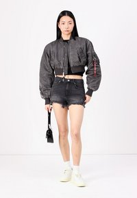 Gray bomber jacket with textured fabric, cropped design, ribbed cuffs, paired with distressed black denim shorts and white sneakers.