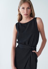 Schwarzes ärmelloses Kleid mit U-Boot-Ausschnitt, geraffter Taille und seitlicher Bindung. Glatter Stoff mit seidigem Glanz. Schlichtes Design, ohne Muster.