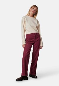 Crème trui gecombineerd met bordeaux corduroy broek. De broek heeft een rechte pijp en een gestructureerd oppervlak, aangevuld met zwarte enkellaarsjes.