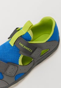 Sandaña de malla azul con detalles en gris, forro verde lima y correa de Velcro. Presenta recortes para ventilación y un talón acolchado.