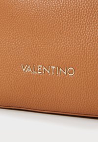 Tan leather handbag featuring a textured surface and gold "VALENTINO" logo. Smooth edges with a rectangular shape.