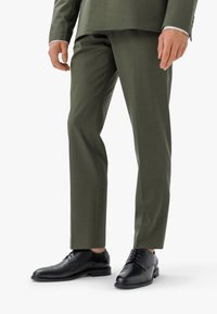 Scarpe eleganti nere in pelle liscia, abbinate a pantaloni verdi oliva su misura. Design aderente con caviglia in vista.