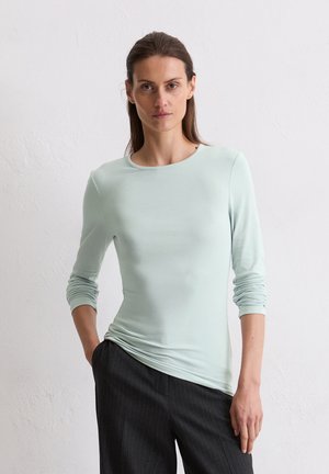 Maglietta a maniche lunghe verde menta chiaro con una texture liscia e scollo a girocollo, abbinata a pantaloni scuri a righe sottili. Design semplice e aderente.