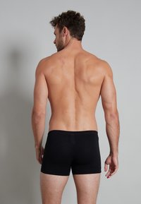 Zwarte bokser shorts met een tailleband met subtiele rode accenten, gemaakt van een zachte stof, met een aansluitend ontwerp en bedekking tot halverwege de dij.
