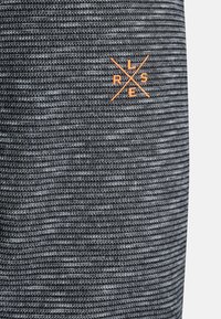 Šedá a černá pletenina s malým oranžovým vyšitým logem, které zobrazuje písmena R, L, S a E uspořádané kolem křížených čar.