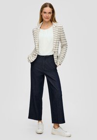 Witte gestreepte blazer over een witte top, gecombineerd met marineblauwe wijde broek en witte sneakers. Strak ontwerp met subtiele textuur.