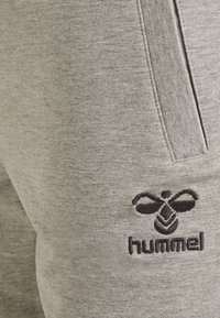 Grå sweatpants med mjuk textur, som har sidofickor och en svart broderad logotyp av en bi med ordet "hummel" under.