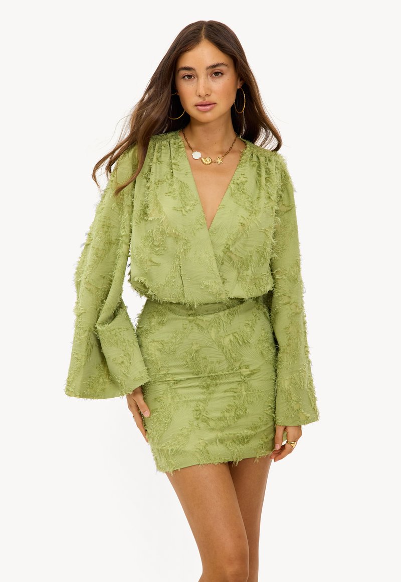 Robe mini texturée verte avec de longues manches en forme de cloche et un décolleté en V profond. Présente une silhouette ajustée et des détails à franges superposées sur l'ensemble.