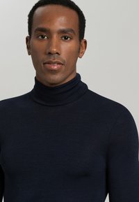 Maglione girocollo navy in tessuto leggero e morbido. Presenta un design aderente con colletto alto e maniche lunghe.