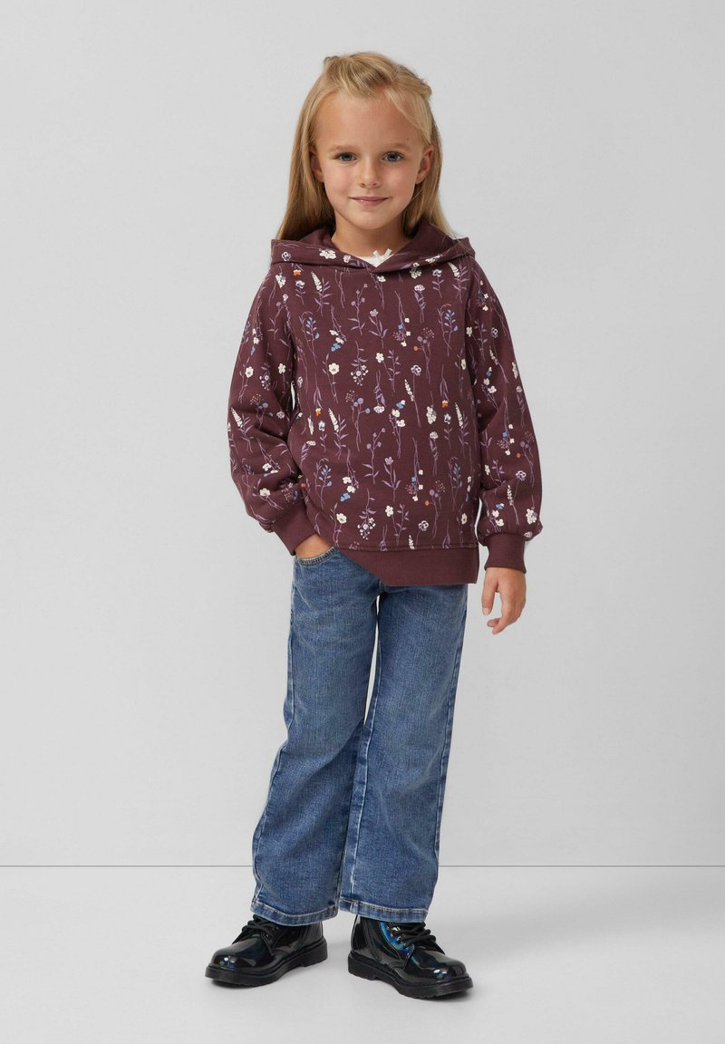 Bordeauxkleurige capuchontrui met bloemmotief, gecombineerd met wijde blauwe jeans en zwarte schoenen. Soepele stof, ontspannen pasvorm en ribgebreide manchetten.
