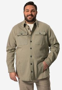 Oliivinvihreä napillinen takki, jossa on kaksi etutaskua ja joka on valmistettu kestävästä kankaasta. Takissa on klassinen kaulus ja näkyvät mustat napit.