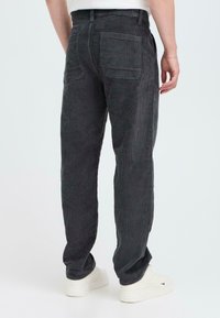 Dark gray corduroy pants with a straight fit, featuring two back pockets and a textured surface, paired with white sneakers.