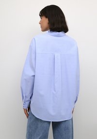 Jasnoniebieska, oversize koszula z bawełny, z pointed kołnierzykiem, opadającymi ramionami, plisą z tyłu i zapięciem na guziki przy mankietach.