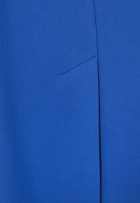 Blaues Gewebe mit einer glatten Textur, dezenten Nähten und einem schrägen Schnitt. Keine sichtbaren Muster oder Beschläge erkennbar.