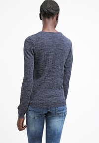Suéter de punto texturizado azul oscuro con mangas largas y escote redondo, combinado con jeans de denim azul desvanecido. Se muestra la vista posterior.