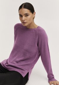 Lila Strickpullover mit langen Ärmeln, Rundhalsausschnitt und strukturierten Schulterdetails. Bietet eine lockere Passform und seitliche Schlitze am Saum.