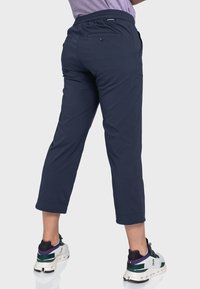 Marineblaue, gekürzte Hosen mit einem Bund, zwei hinteren Taschen mit Knöpfen und einer glatten Textur, kombiniert mit weißen und grünen Sportschuhen.