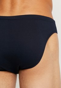 Mutande da bagno in cotone blu navy scuro, con texture liscia, design a copertura minima, con schiena arrotondata e bordatura cucita per una maggiore durata.
