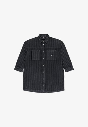 Maglietta a righe bianche e nere a maniche lunghe con colletto abbottonato e due tasche frontali, con una patch del logo sul lato sinistro.