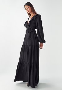 Black maxi dress with ruffled neckline and long sleeves. Soft fabric, cinched waist with a tie, and tiered skirt design.
