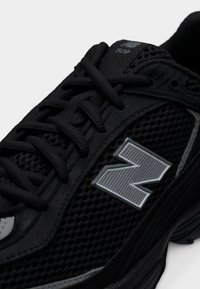 Baskets noires New Balance 509 en tissu mesh, lacets épais et grand logo gris "N" sur le côté.