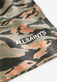 Tkanina s kamuflažnim uzorkom u zelenoj, smeđoj i narančastoj boji s "ALLSAINTS" i "LONDON" natpisima u bijeloj boji. Glatka tekstura, moderni dizajn.