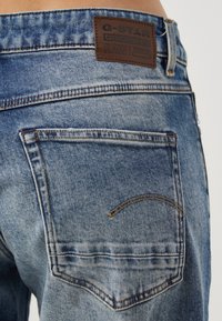 Primer plano del bolsillo trasero de unos vaqueros de mezclilla azul descolorida con una etiqueta de cuero marrón de la marca G-Star Originals en la pretina.